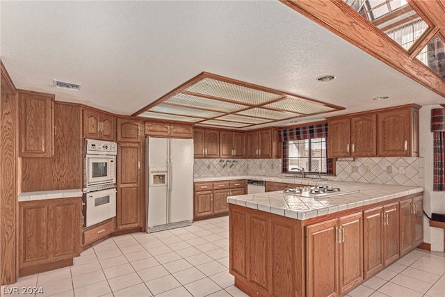 kitchen featuring light tile floors, kitchen peninsula, tasteful backsplash, white appliances, and tile counters