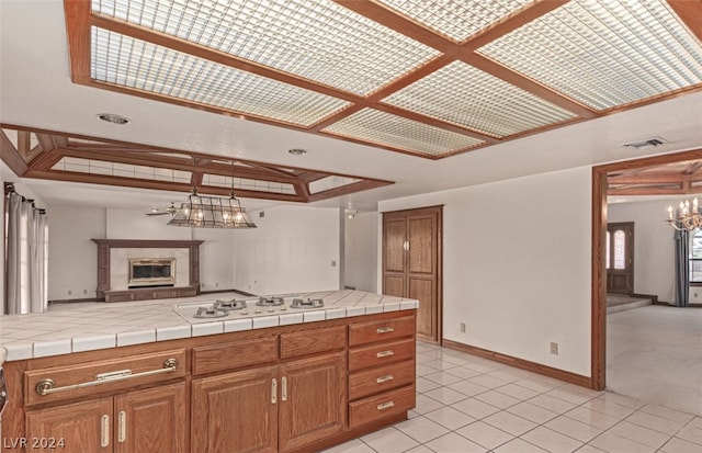 kitchen with an inviting chandelier, a tiled fireplace, light carpet, white gas stovetop, and tile countertops