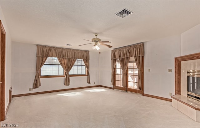 unfurnished living room featuring ceiling fan, a textured ceiling, a tile fireplace, and light colored carpet