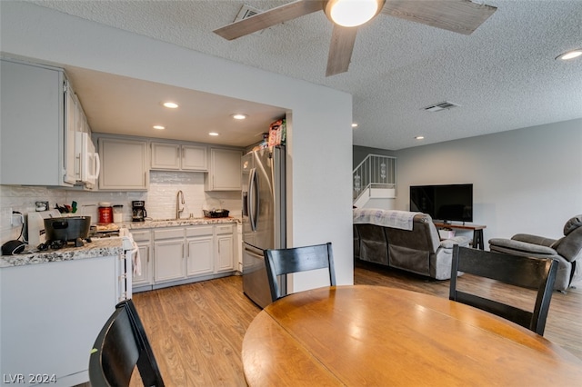 dining area with a textured ceiling, sink, ceiling fan, and light wood-type flooring