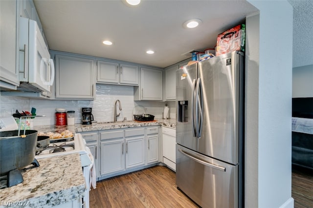 kitchen with sink, white appliances, backsplash, light hardwood / wood-style flooring, and light stone countertops