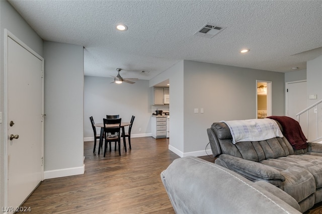 living room with dark hardwood / wood-style flooring, ceiling fan, and a textured ceiling