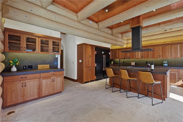 kitchen featuring island range hood, built in refrigerator, a kitchen island, and a breakfast bar