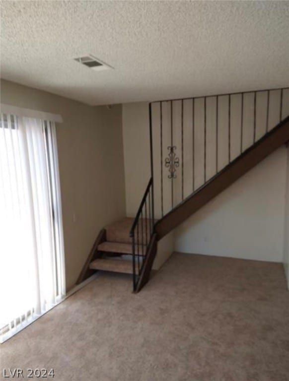 stairway with light carpet, a textured ceiling, and plenty of natural light