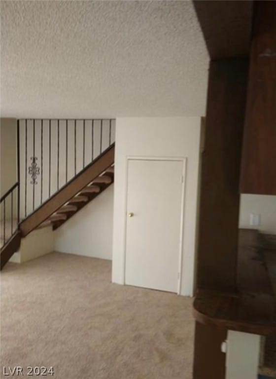 stairs with a textured ceiling and light colored carpet