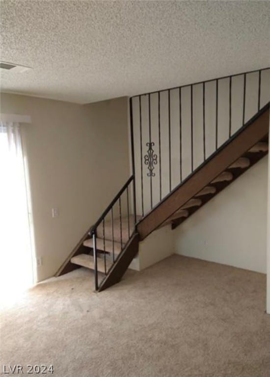 staircase with a textured ceiling and light colored carpet