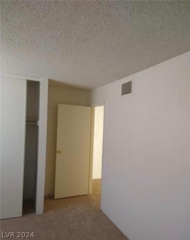 unfurnished bedroom with a textured ceiling and light colored carpet