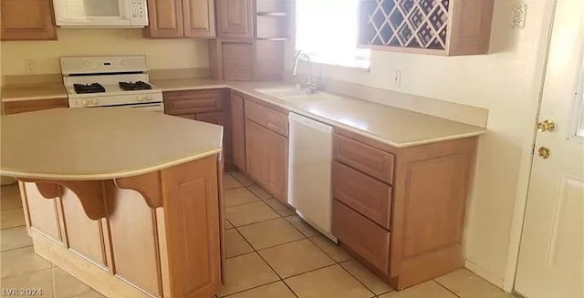 kitchen featuring white appliances, sink, light tile floors, and a kitchen bar