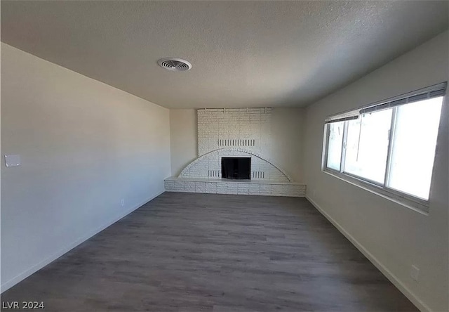 unfurnished living room featuring brick wall, dark hardwood / wood-style floors, a brick fireplace, and a textured ceiling