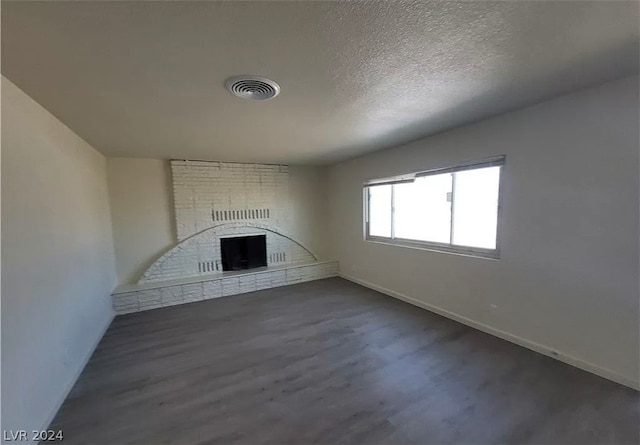 unfurnished living room with brick wall, a textured ceiling, dark hardwood / wood-style flooring, and a fireplace