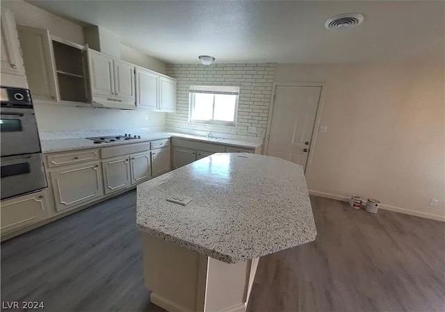 kitchen with light stone countertops, a kitchen island, black double oven, and dark hardwood / wood-style flooring