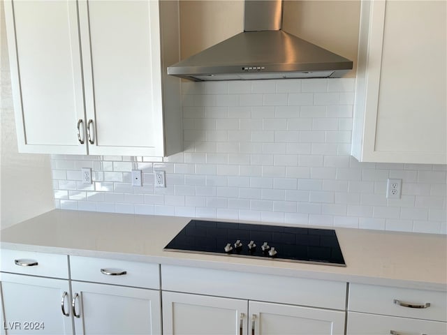 kitchen featuring wall chimney exhaust hood, black electric stovetop, and white cabinetry