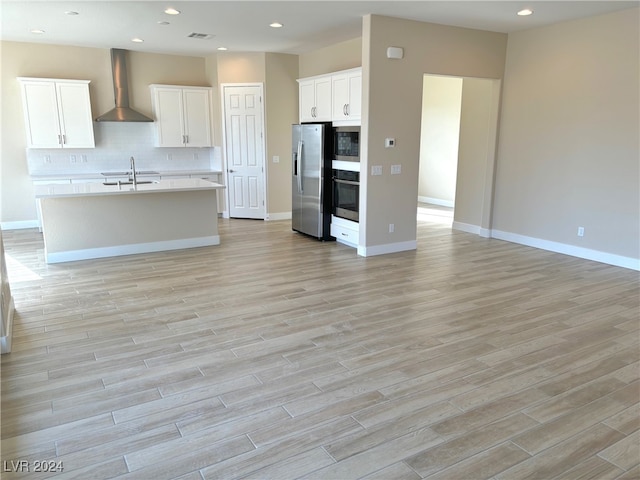 kitchen with wall chimney range hood, light hardwood / wood-style flooring, stainless steel appliances, sink, and white cabinets