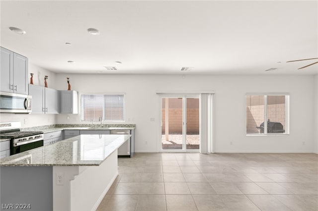 kitchen featuring ceiling fan, light tile floors, light stone counters, stainless steel appliances, and a center island