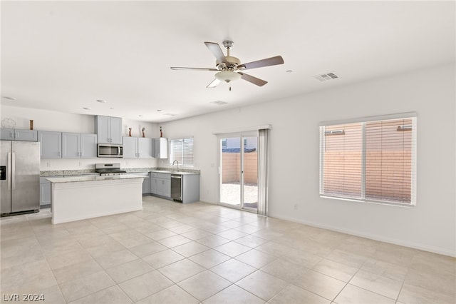 kitchen with gray cabinetry, ceiling fan, stainless steel appliances, light tile floors, and a center island