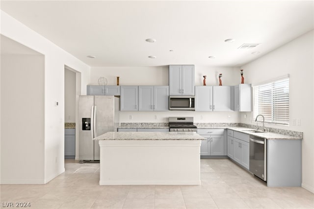 kitchen featuring sink, light tile floors, light stone counters, stainless steel appliances, and a center island