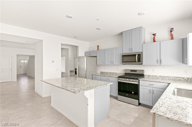 kitchen featuring appliances with stainless steel finishes, light stone counters, light tile floors, gray cabinets, and a center island