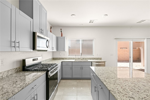 kitchen featuring stainless steel appliances, light tile floors, gray cabinets, light stone counters, and sink