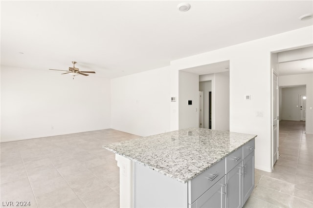 kitchen with ceiling fan, light tile flooring, a center island, and light stone countertops