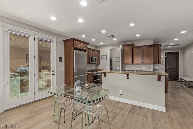 kitchen with a breakfast bar, light stone counters, appliances with stainless steel finishes, and light hardwood / wood-style flooring