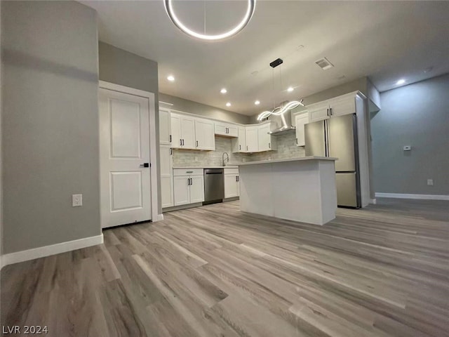 kitchen with appliances with stainless steel finishes, decorative light fixtures, white cabinets, and light hardwood / wood-style flooring