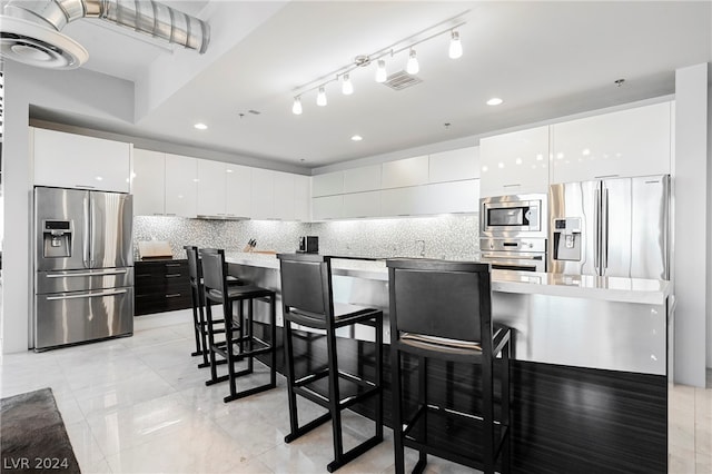 kitchen with light tile floors, white cabinets, a breakfast bar, stainless steel appliances, and tasteful backsplash