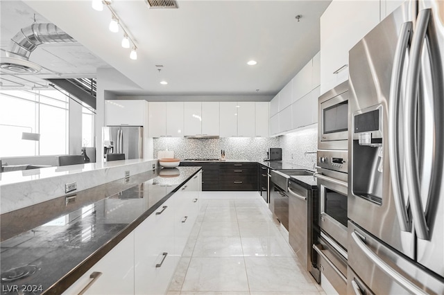 kitchen with tasteful backsplash, white cabinets, appliances with stainless steel finishes, and dark stone counters