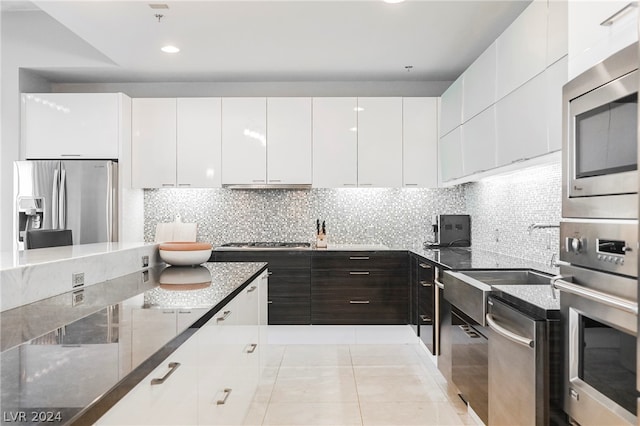 kitchen featuring light tile floors, dark stone counters, tasteful backsplash, appliances with stainless steel finishes, and white cabinets