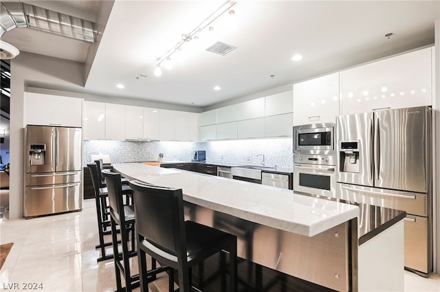 kitchen with appliances with stainless steel finishes, backsplash, a kitchen breakfast bar, and white cabinetry