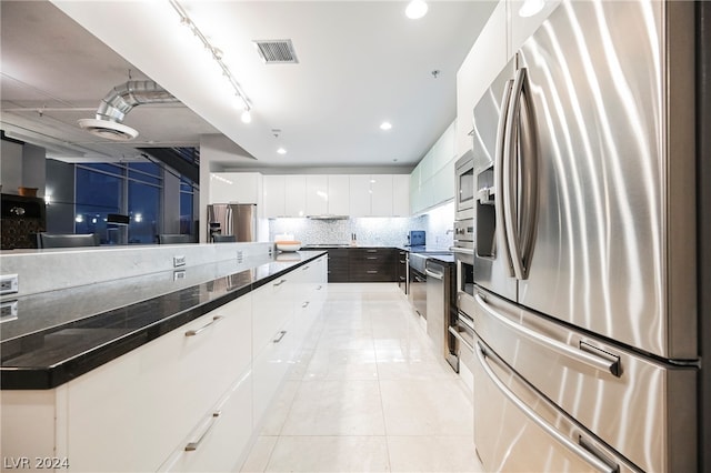 kitchen with dark stone counters, tasteful backsplash, white cabinets, light tile floors, and stainless steel appliances