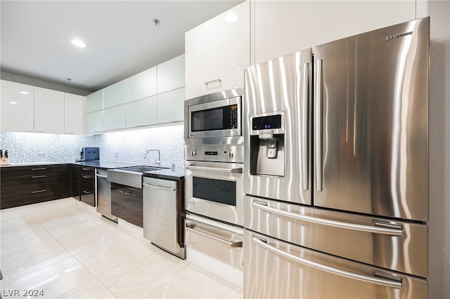 kitchen featuring appliances with stainless steel finishes, light tile flooring, backsplash, sink, and white cabinets