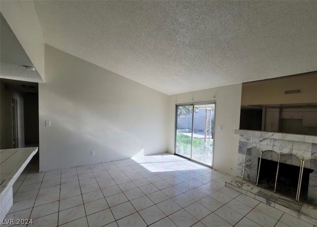 unfurnished living room with a tiled fireplace, light tile flooring, and a textured ceiling