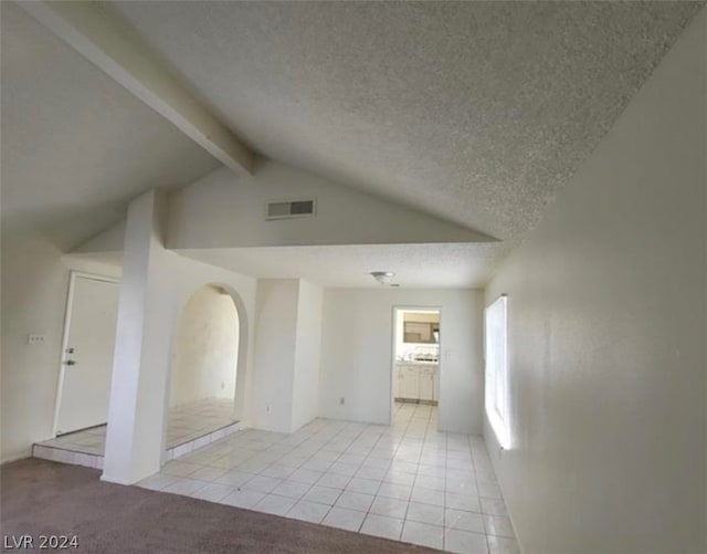 tiled empty room with lofted ceiling with beams and a textured ceiling