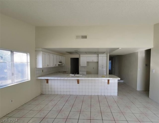 kitchen with kitchen peninsula, a textured ceiling, light tile flooring, and white cabinets