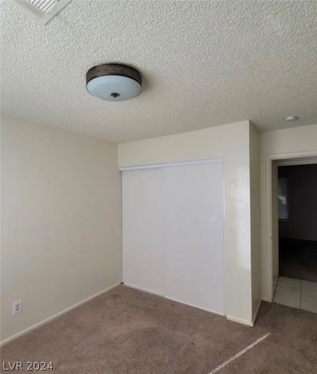 unfurnished bedroom featuring a textured ceiling, a closet, and dark colored carpet