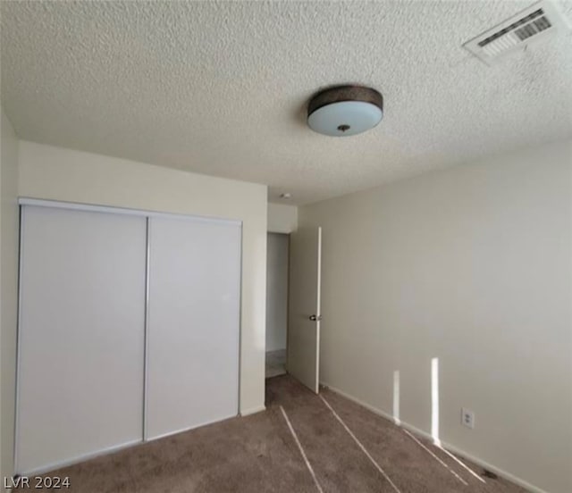 unfurnished bedroom with a closet, a textured ceiling, and dark colored carpet