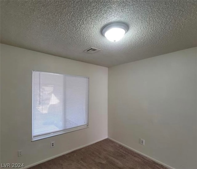 empty room featuring a textured ceiling and dark carpet