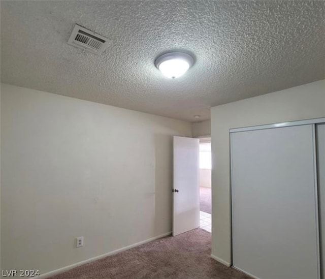 unfurnished bedroom featuring a textured ceiling, a closet, and dark colored carpet