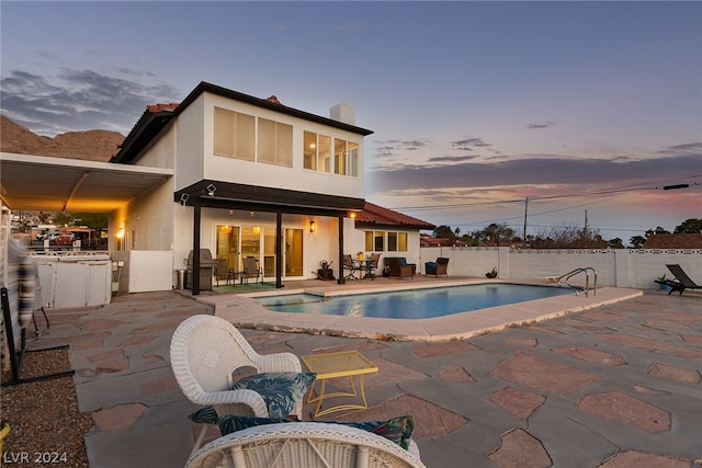 back of property at dusk with a patio area, a fenced backyard, a fenced in pool, and stucco siding