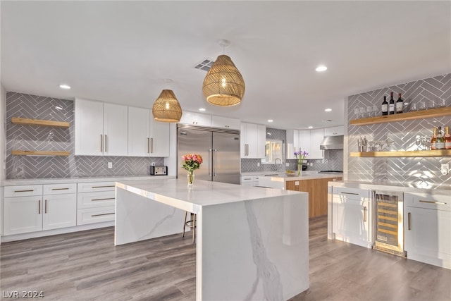 kitchen featuring stainless steel built in refrigerator, white cabinets, a kitchen island, and decorative light fixtures