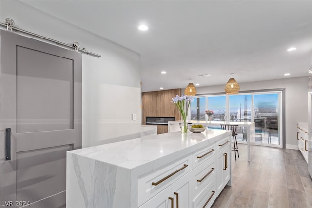 kitchen with a barn door, a kitchen island, light stone counters, and white cabinets