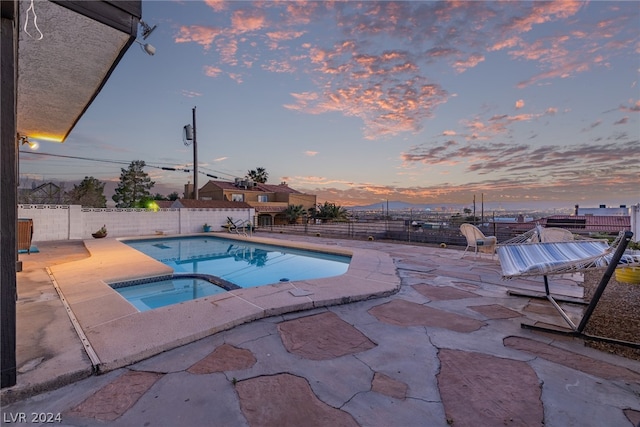 pool at dusk featuring a pool with connected hot tub, a fenced backyard, and a patio