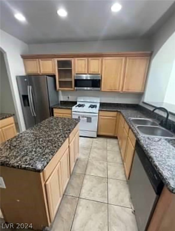 kitchen with appliances with stainless steel finishes, light tile patterned flooring, sink, and dark stone counters