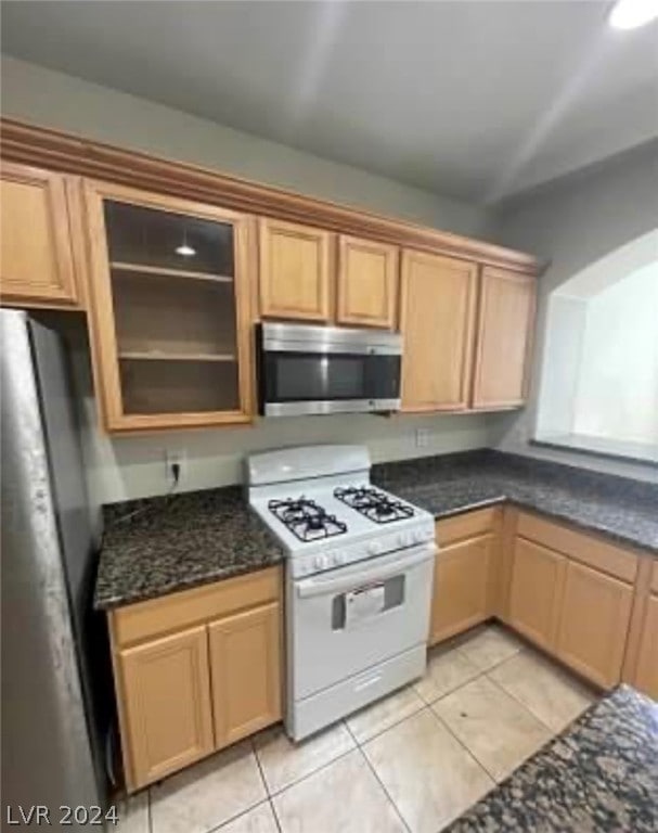 kitchen featuring stainless steel appliances, dark stone countertops, and light tile patterned floors