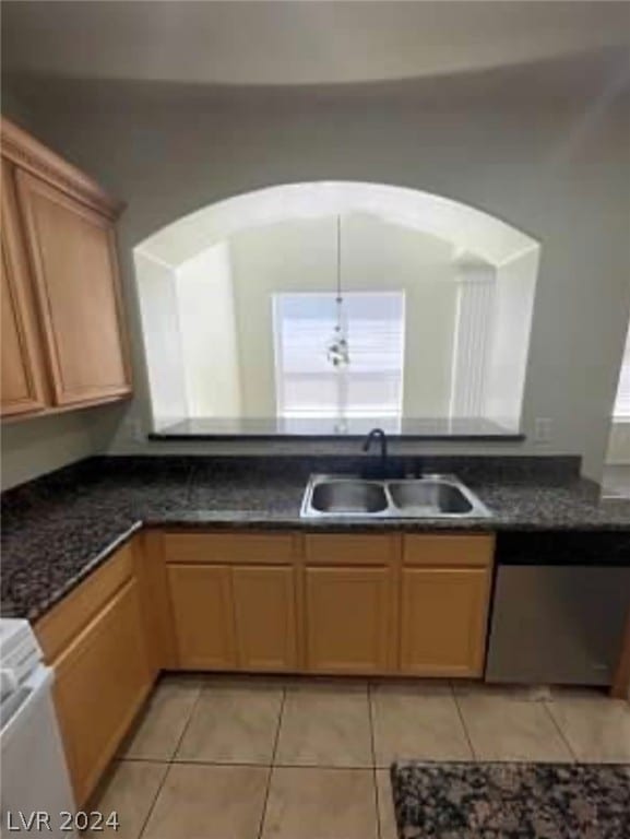 kitchen with dark stone countertops, stainless steel dishwasher, sink, and light tile patterned floors