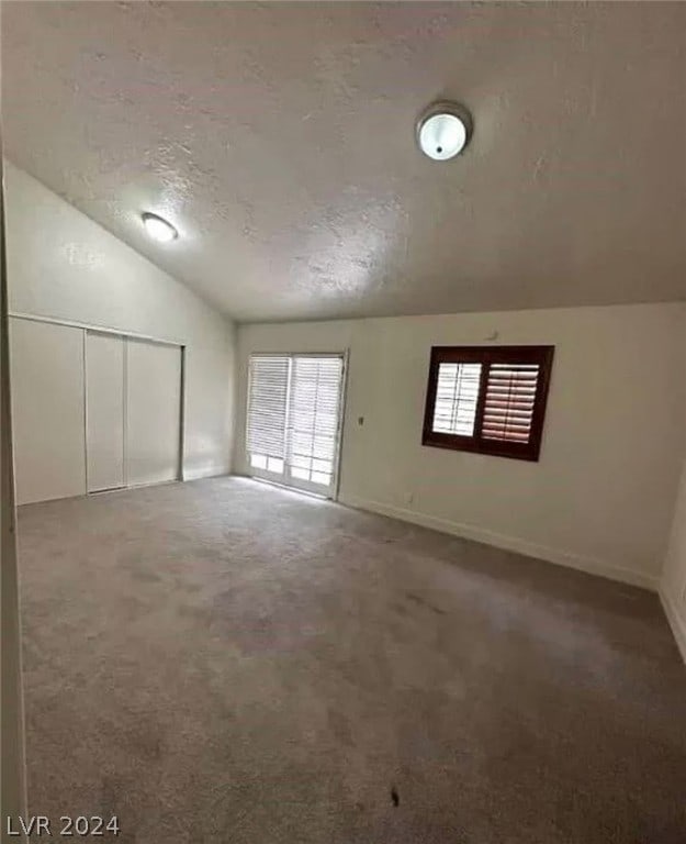 unfurnished room with a textured ceiling, carpet floors, and vaulted ceiling