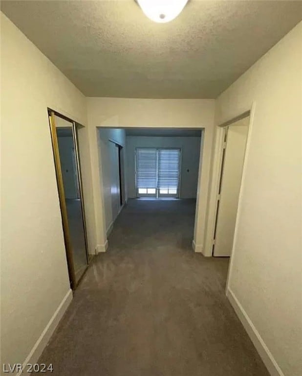 hall featuring dark carpet and a textured ceiling