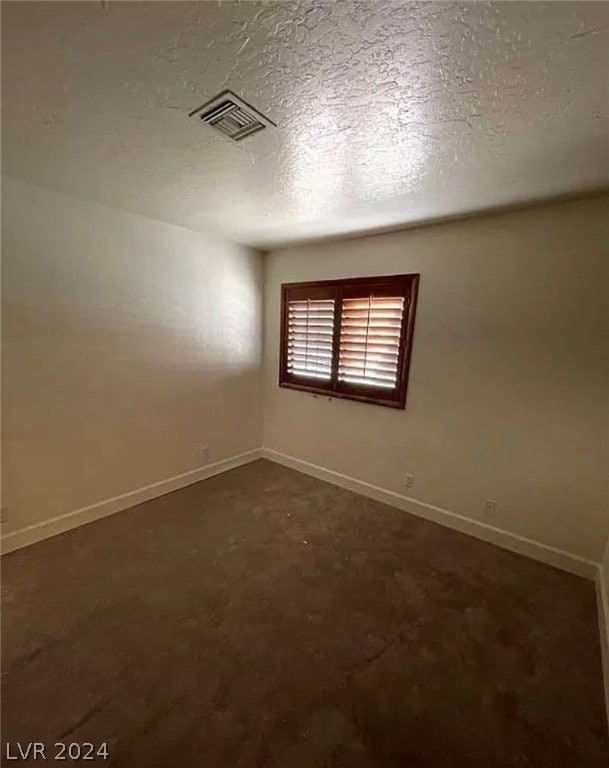 spare room with dark colored carpet and a textured ceiling