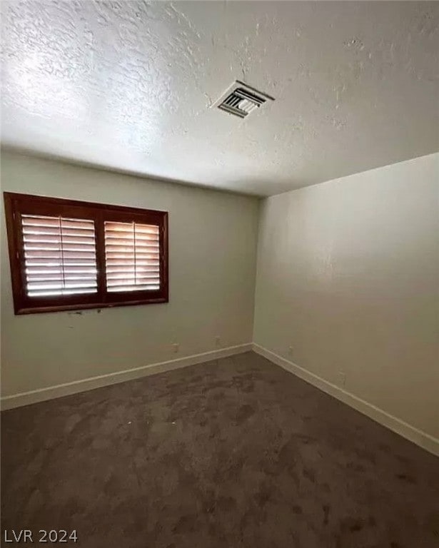 spare room with a textured ceiling and dark carpet