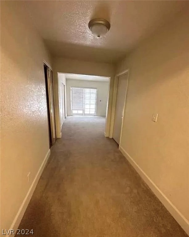 corridor with a textured ceiling and light carpet